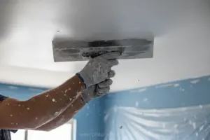 Mãos aplicando massa corrida no teto com desempenadeira