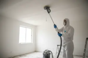 Pessoa lixando teto com lixadeira de longo alcance e aspirador de pó.